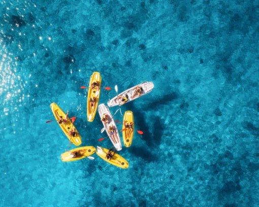 Aerial view of yellow kayaks in blue sea at sunset in summer. People on floating canoes in clear azure water. Sardinia island, Italy. Tropical landscape. Sup boards. Active travel. Top view from drone