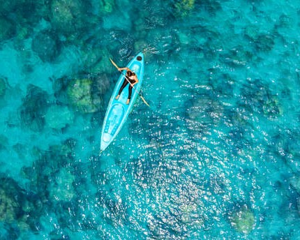 Aerial view of a woman kayaking in the blue sea and clear water. You can see corals under the sea.